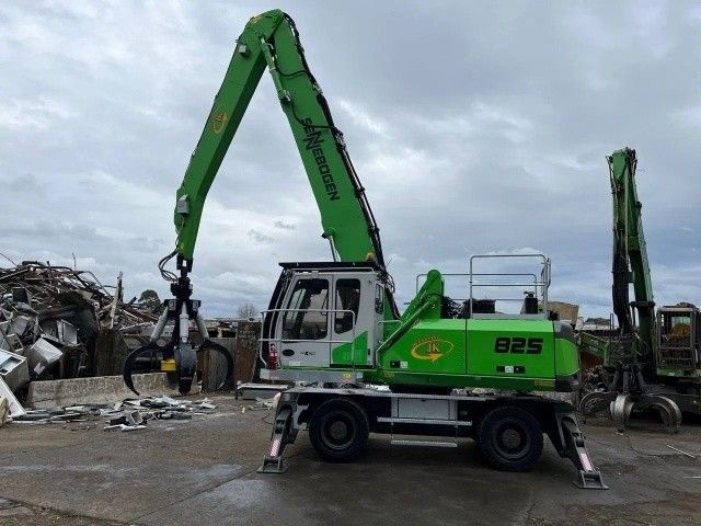A green JK Recycling crane stands besides a large pile of scrap metal in an industrial setting. A green JK Recycling crane stands besides a large pile of scrap metal in an industrial setting.