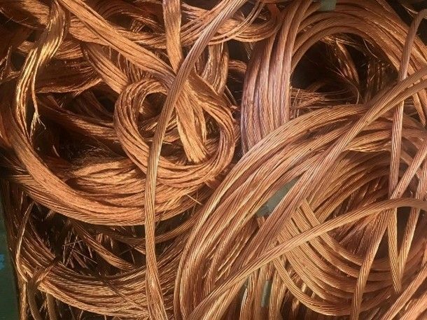A green bin filled with a pile of copper wire, showcasing its metallic sheen and tangled form.