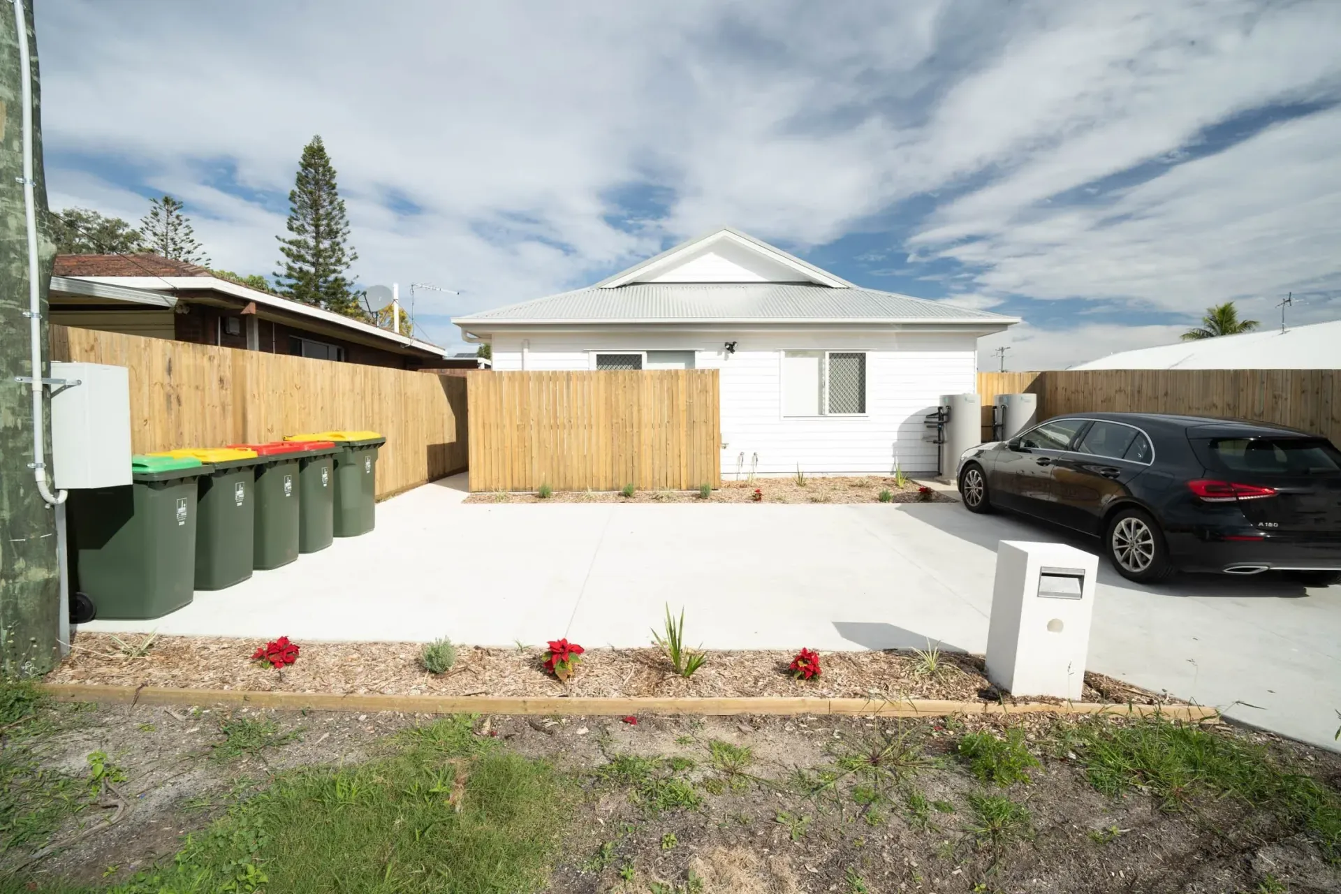 Front of a completed rooming house with a white roof and a timber fence