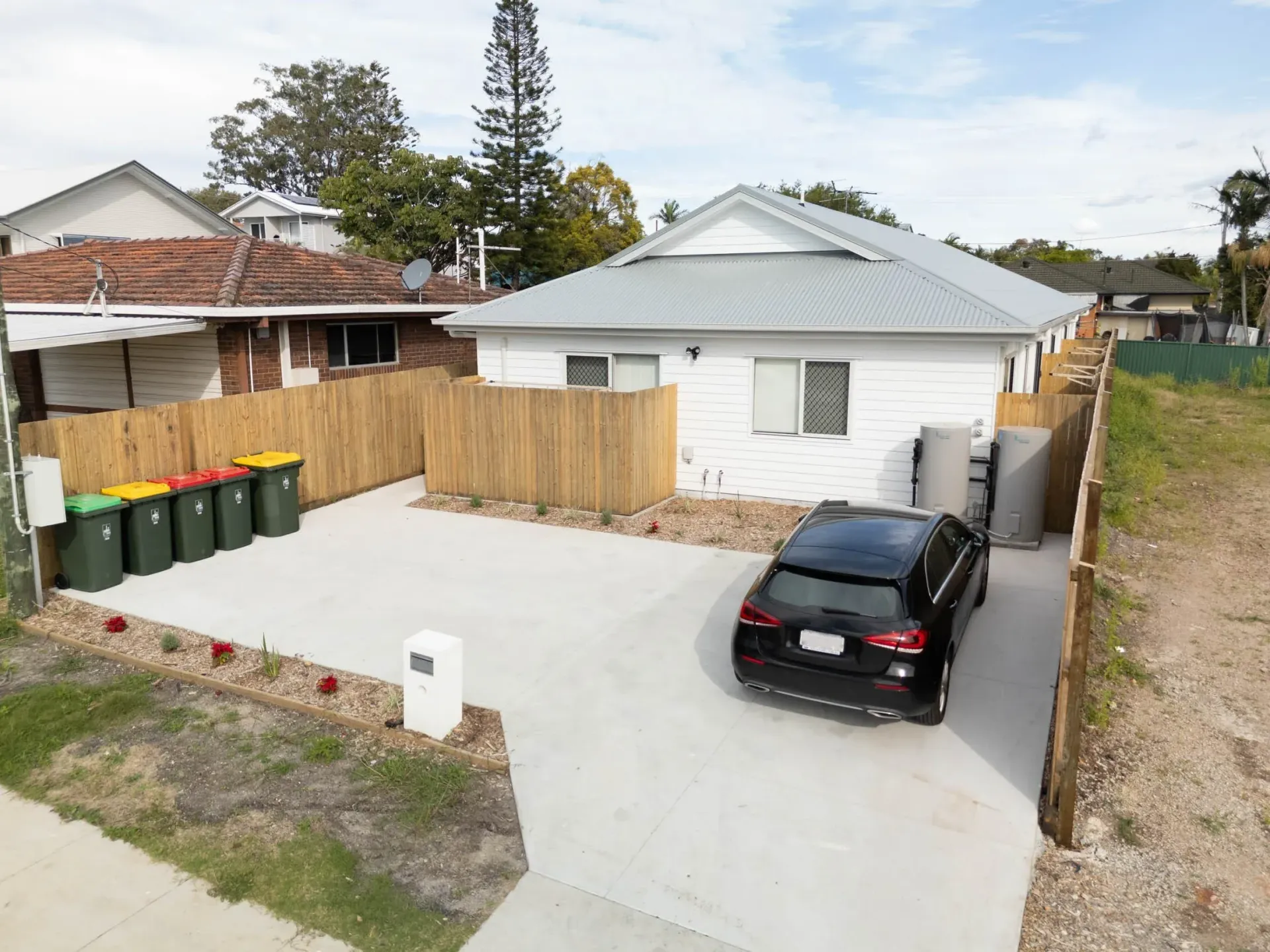 Completed rooming house from the street, with driveway, bins and a timber fence