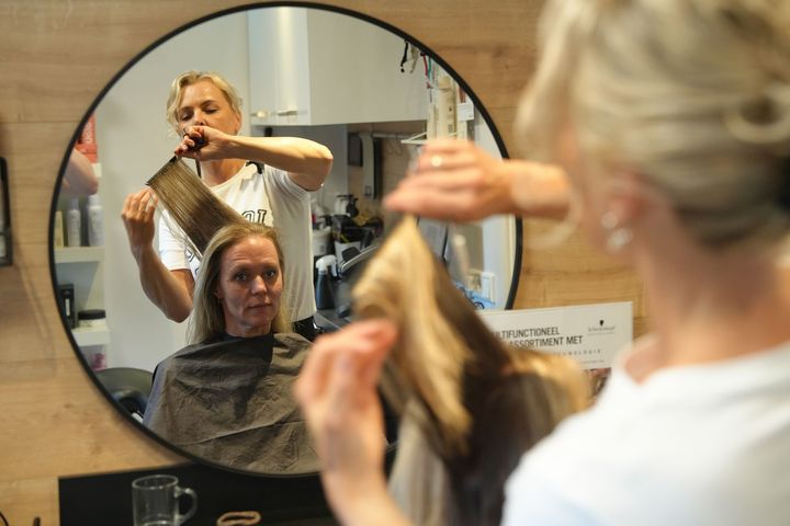 Een kapper stylt het haar van een zittende klant in een salonspiegel.