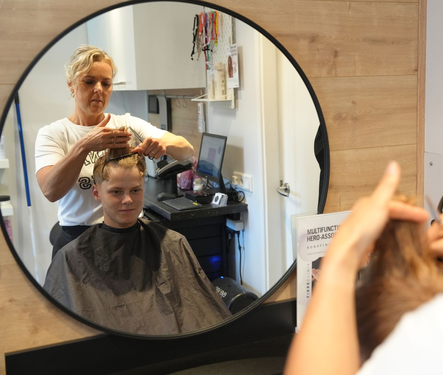 Een kapper knipt het haar van een klant voor een spiegel in een kapsalon.