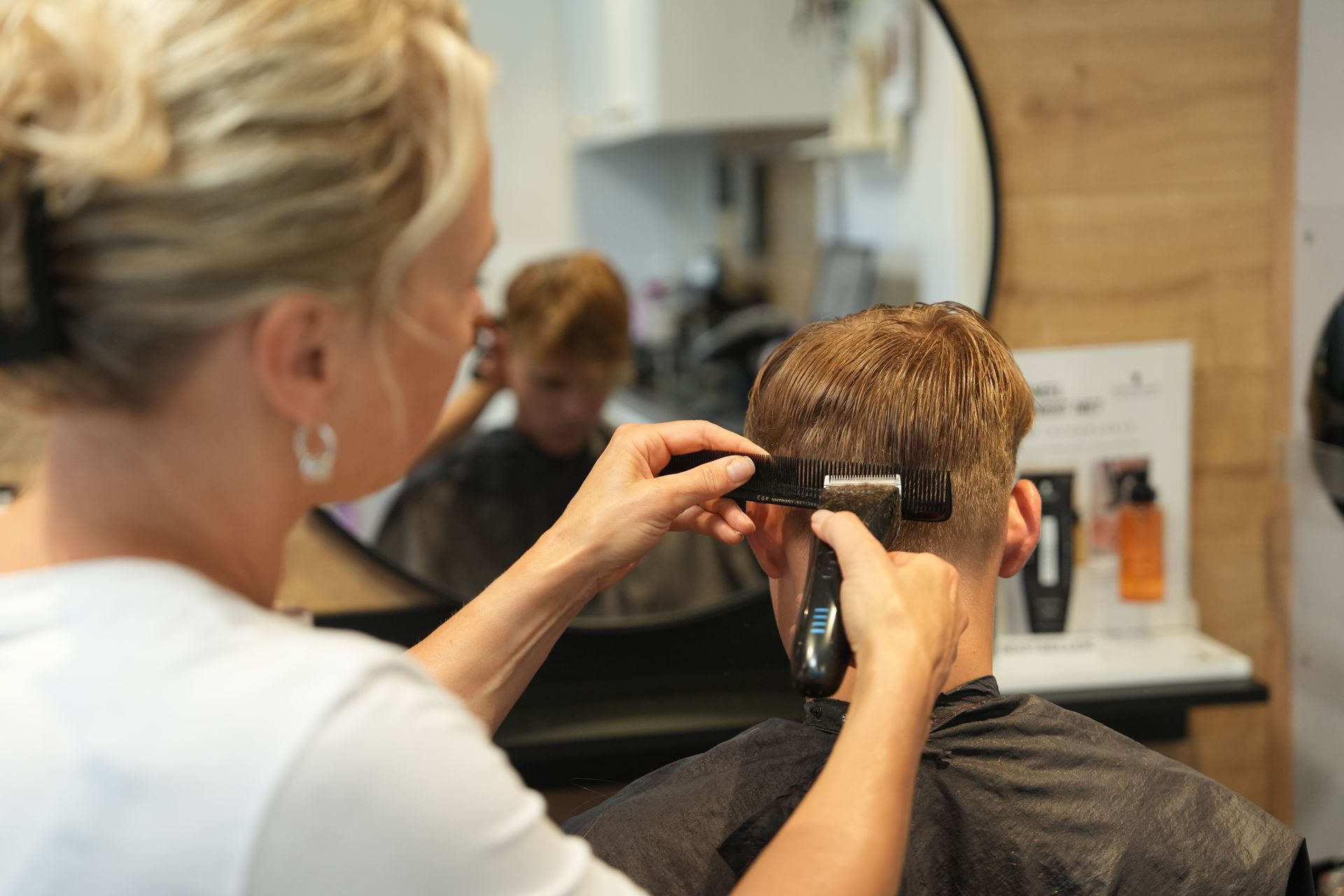 Een stylist knipt het haar van een klant bij met een tondeuse in een salon.