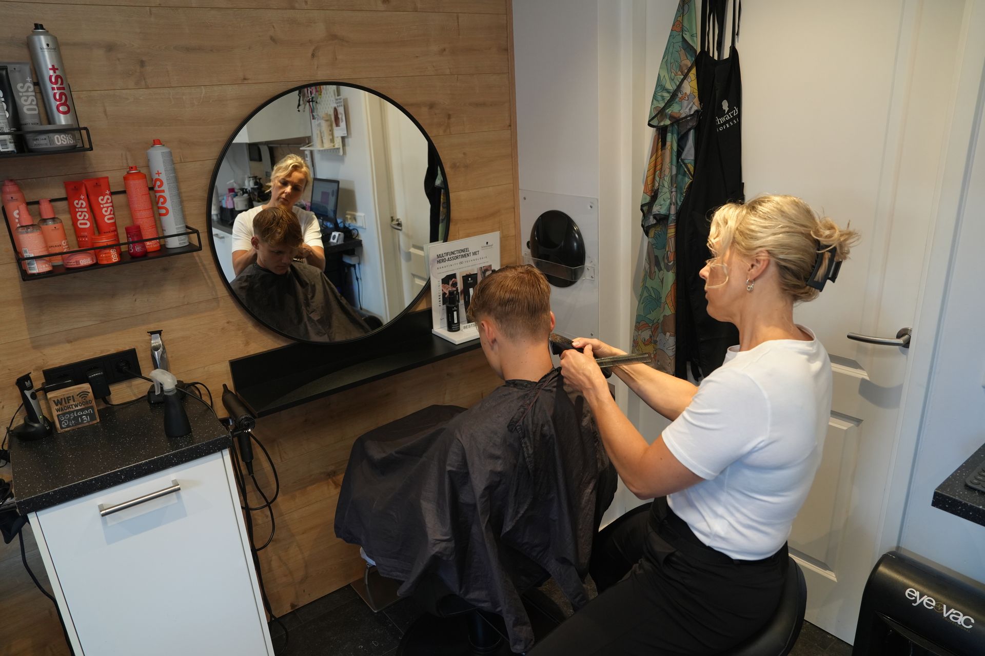 Een kapper knipt het haar van een klant in een salon met een spiegel en een kappersstoel.