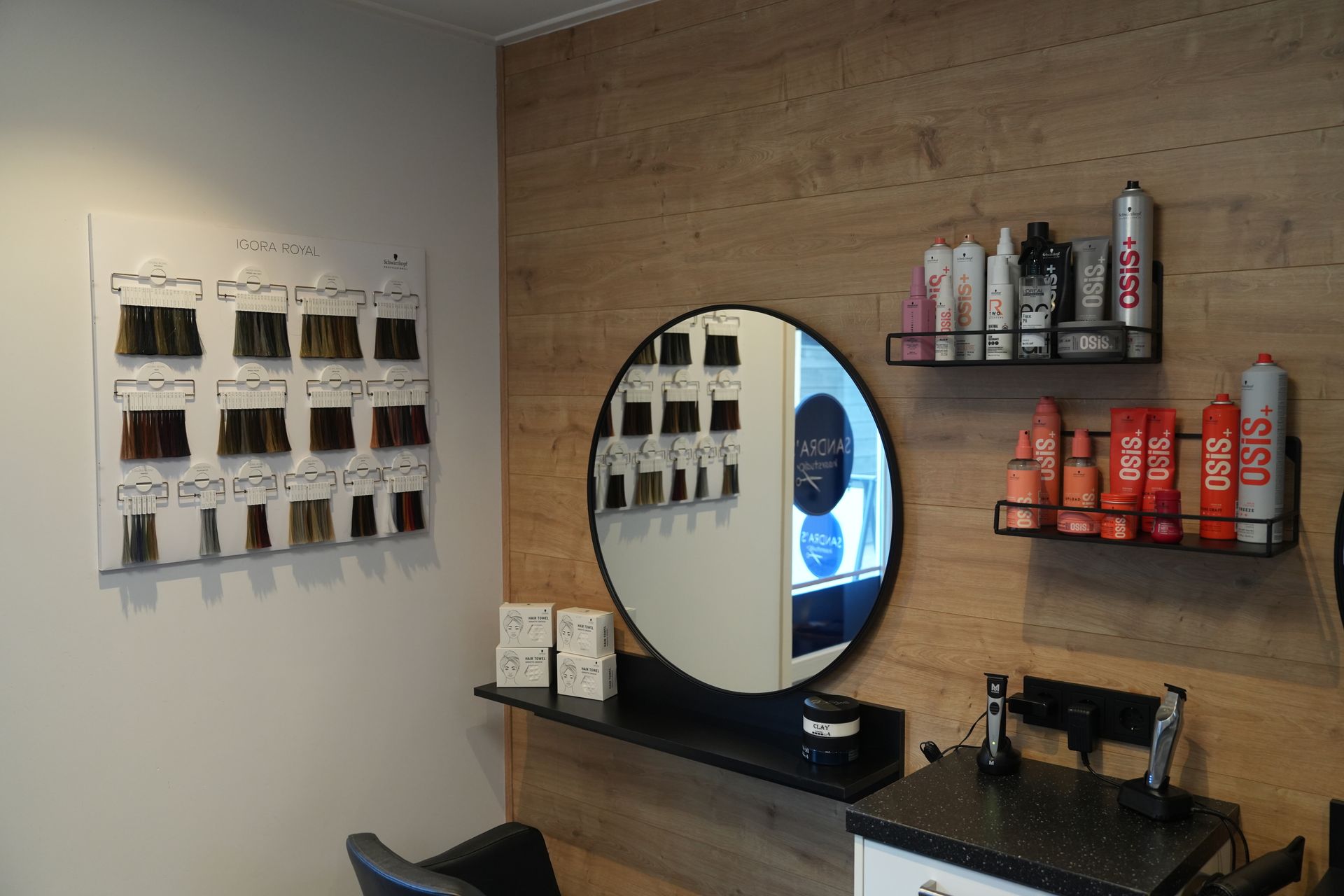 Salonstoel met spiegel, productplanken en haarkleurstalen aan de muur.