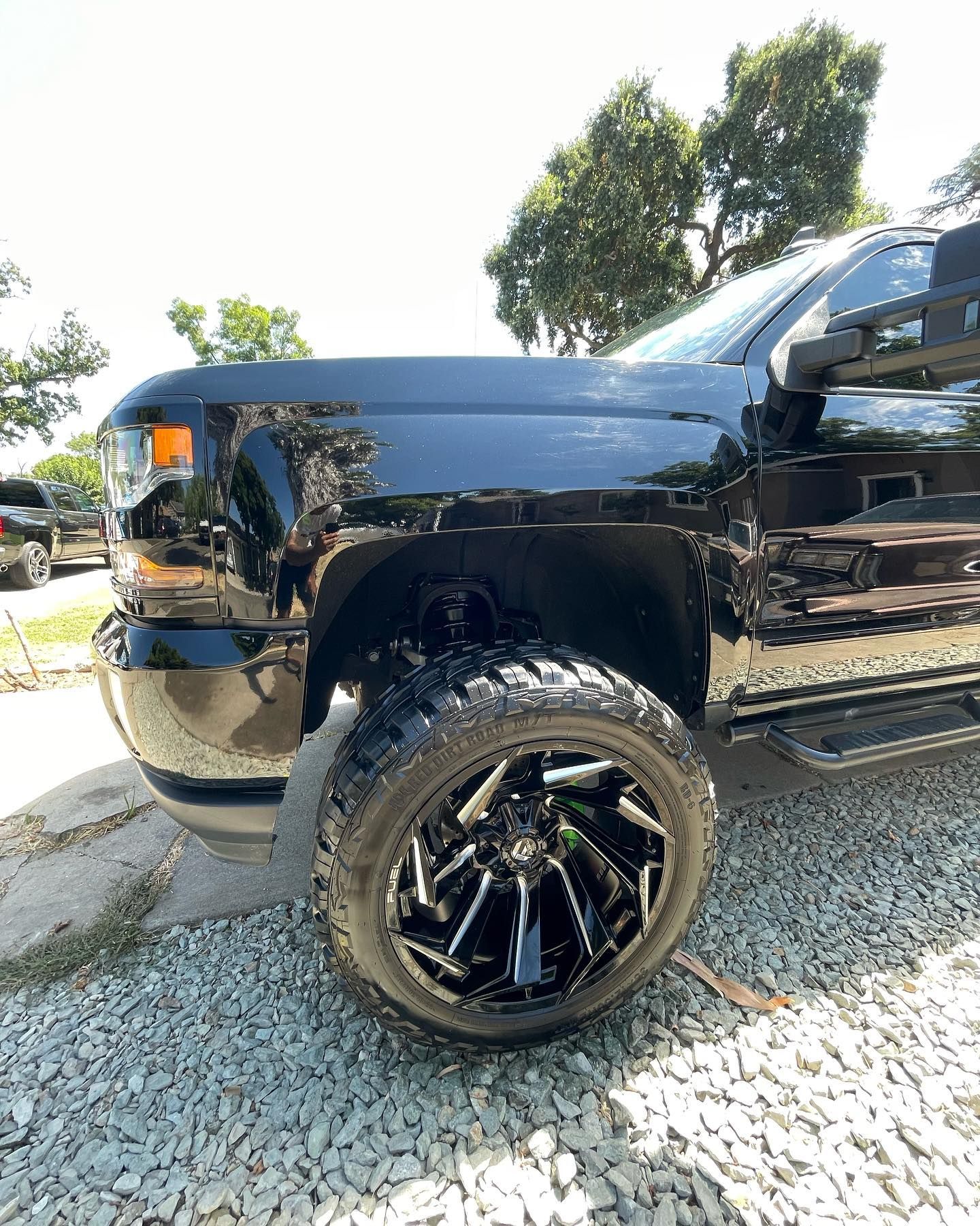 A black truck is parked on gravel next to a road.