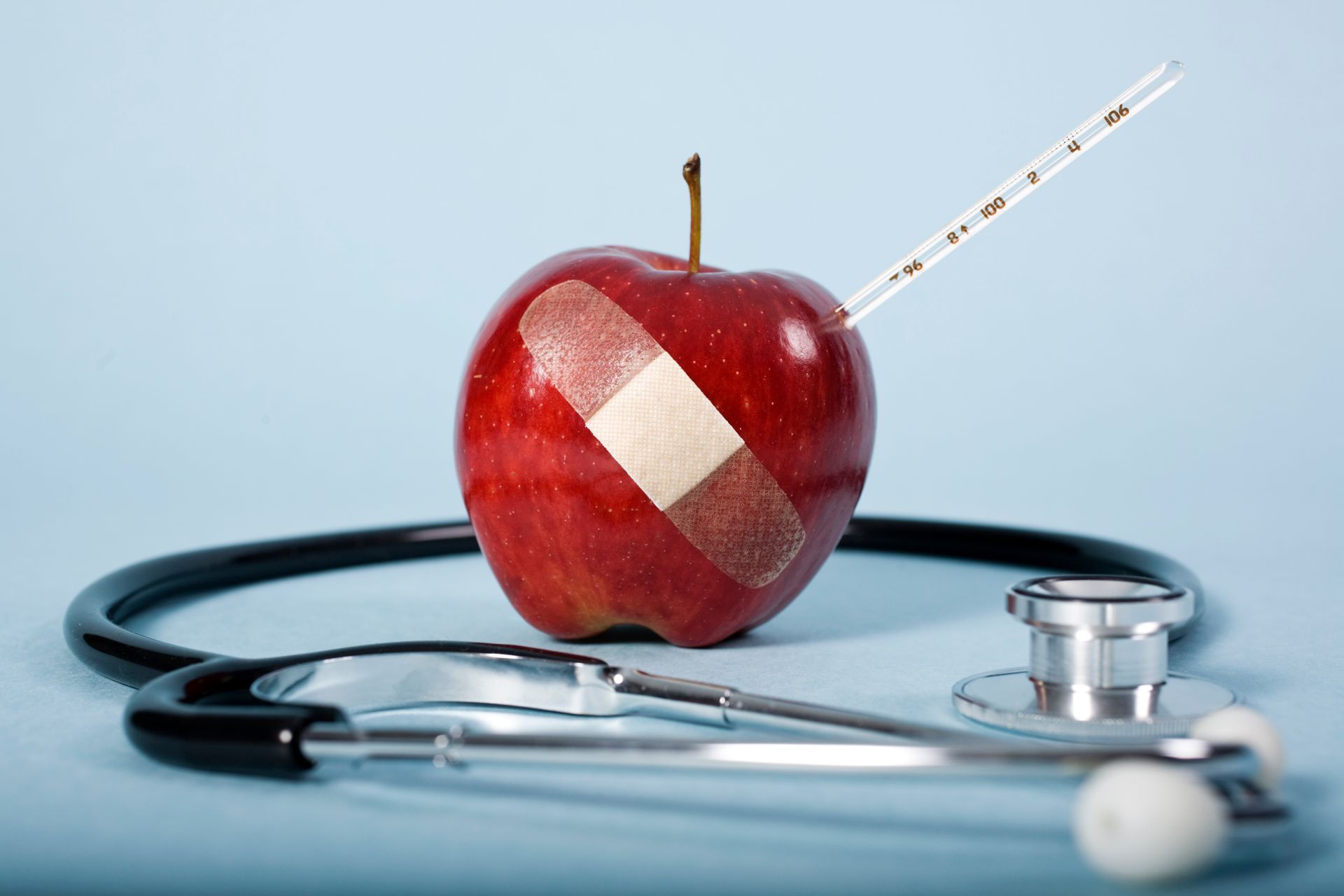 An apple with a bandage is on a table with a stethoscope