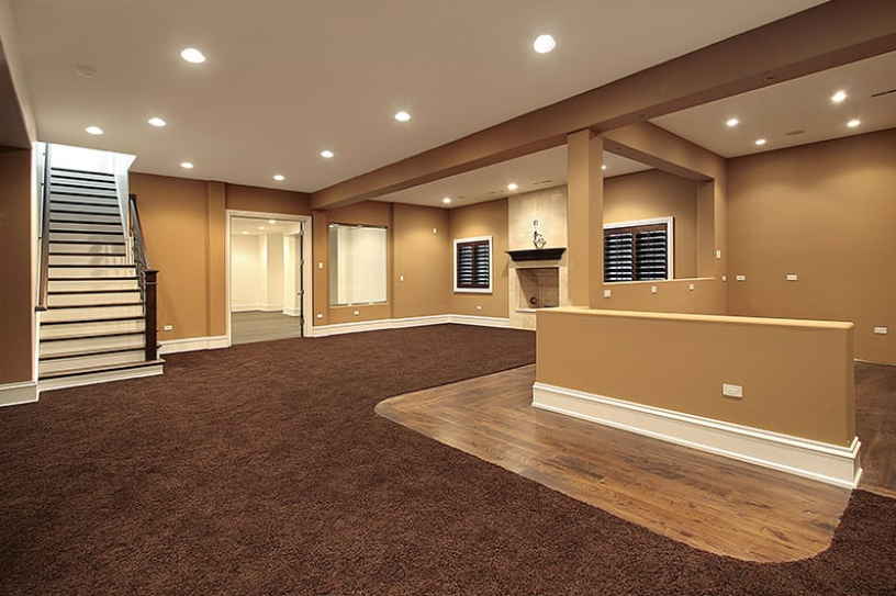 Empty finished basement with carpeted living area, stairs, recessed lights, and a small bar counter.