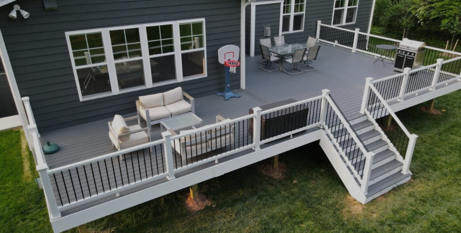 Back deck with gray railing, outdoor seating, stairs, and a basketball hoop beside a house