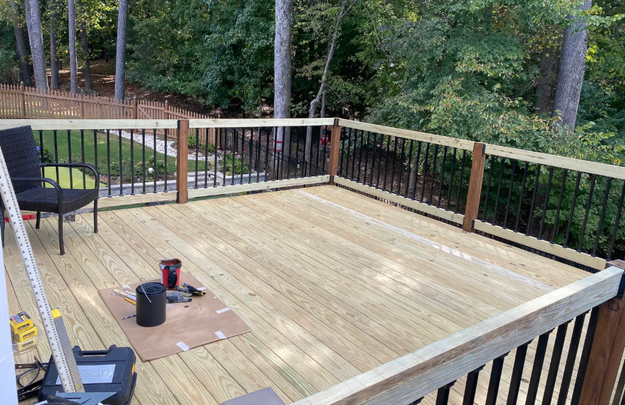 Wooden deck under construction with railings, tools, and chairs overlooking trees