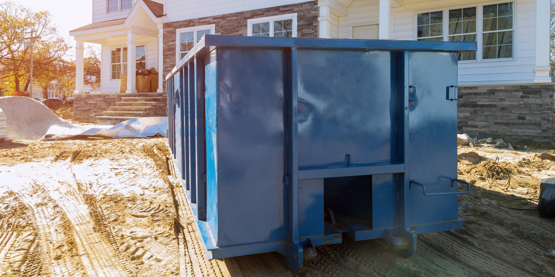 Blue dumpster on a snowy driveway beside a house