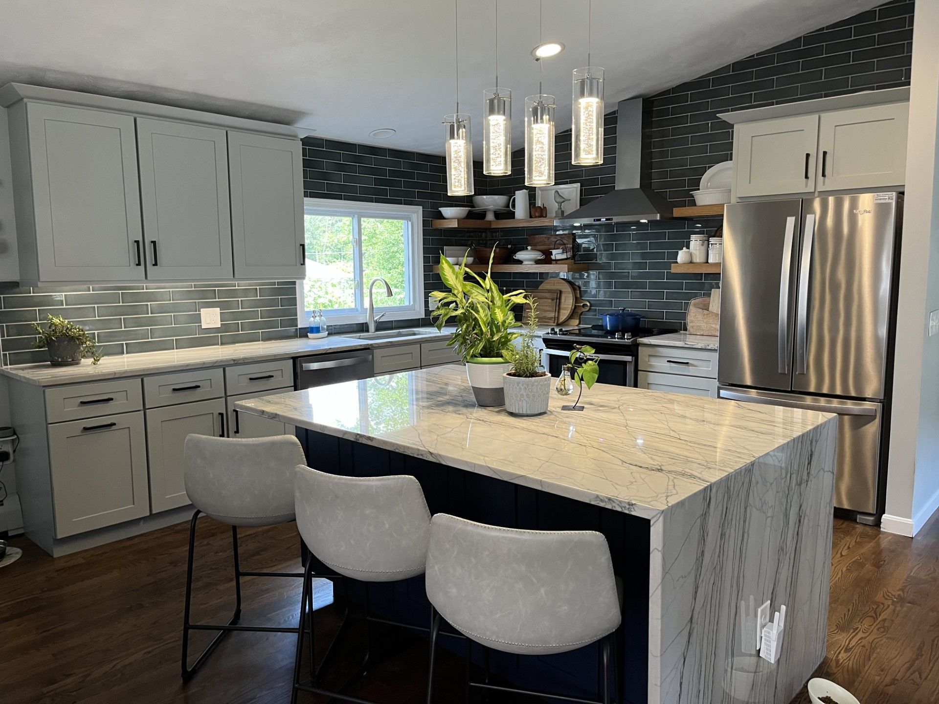Modern kitchen with gray cabinets, stainless fridge, marble island, and pendant lights