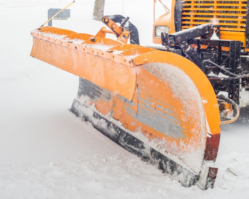 Orange snowplow clearing heavy snow on a road during a snowfall