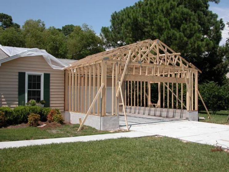 House with a wooden garage/frame under construction beside a driveway and lawn