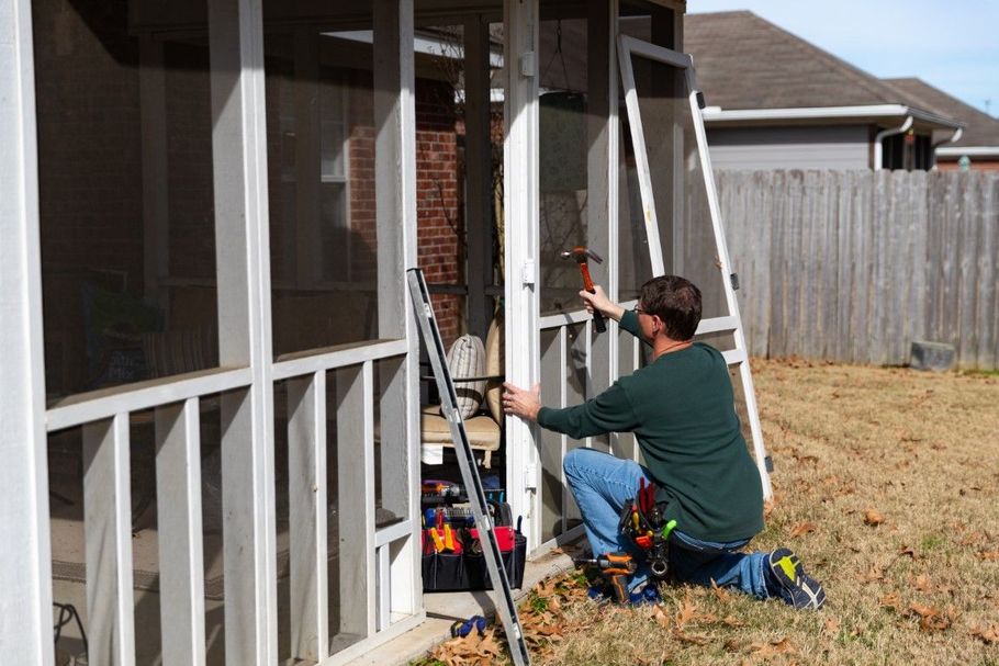 Person on a ladder painting a house exterior beside a screened porch