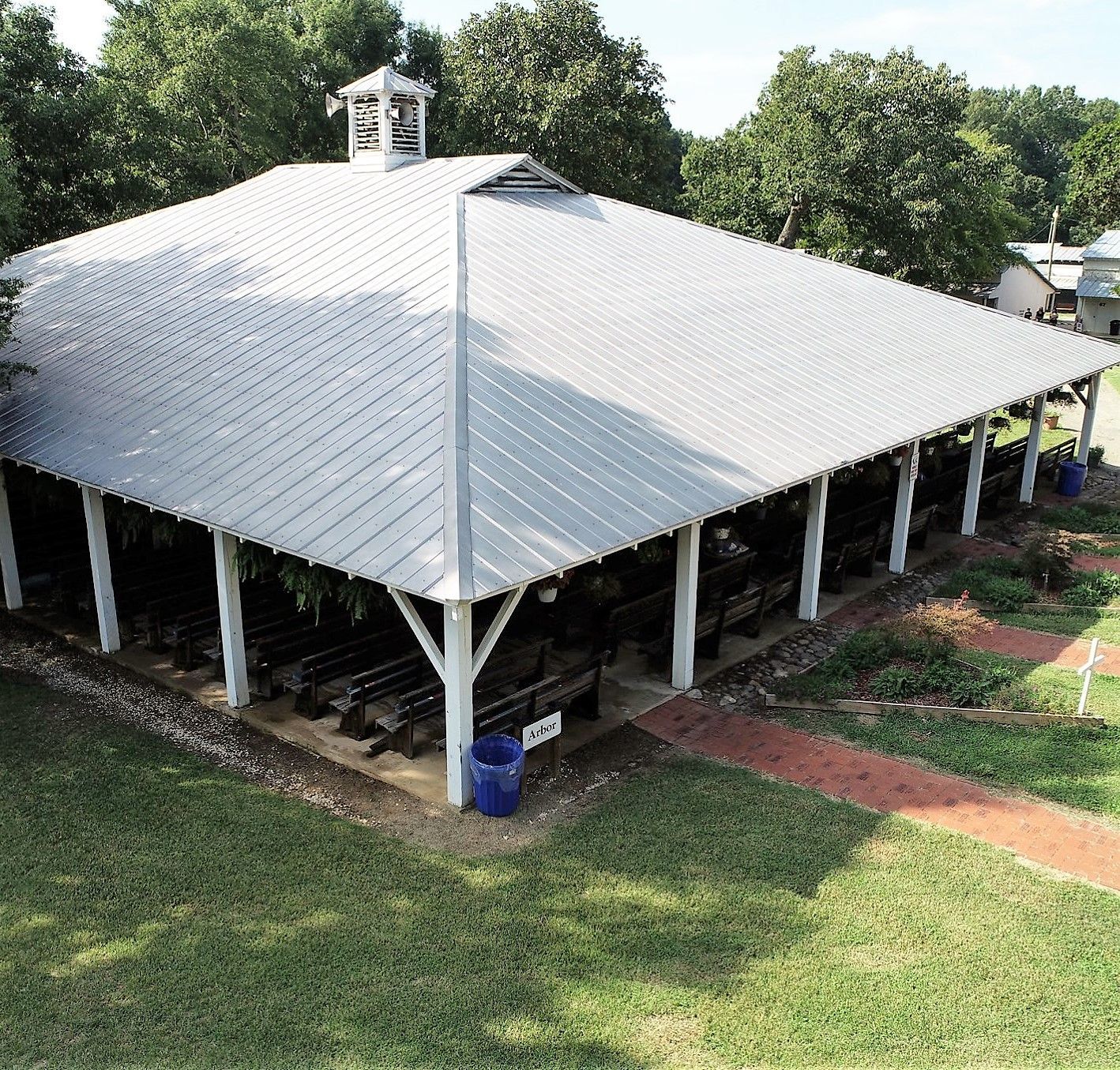 Large white-roofed pavilion on stilts in a grassy area, viewed from above.