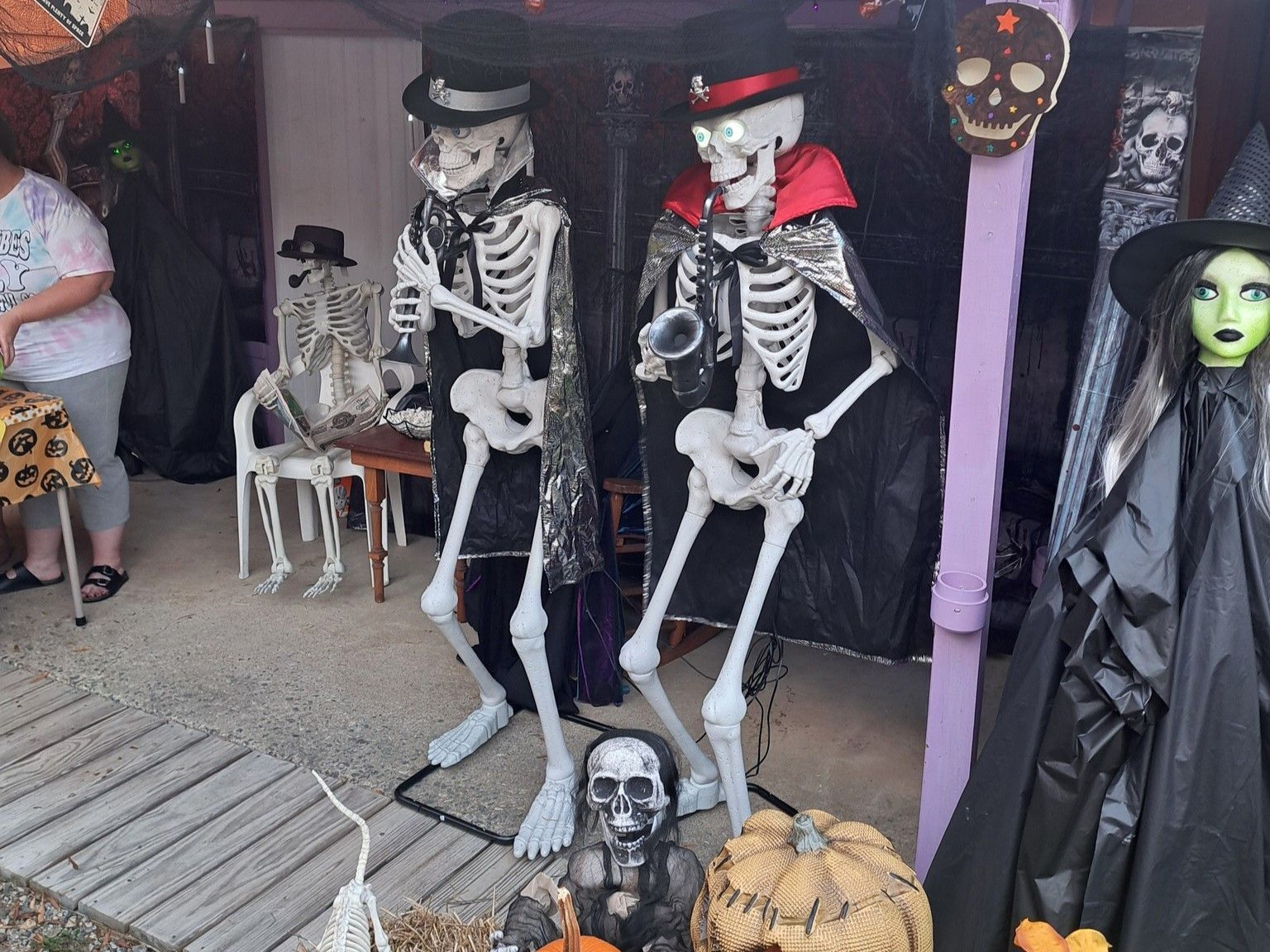 Halloween yard display with two skeletons, pumpkins, skull decor, and a green-faced witch figure by a porch