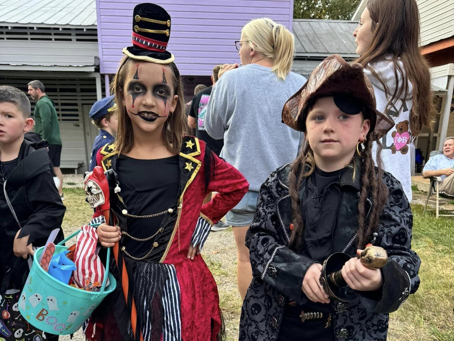 Two children in Halloween costumes at an outdoor event, one holding a candy bucket.