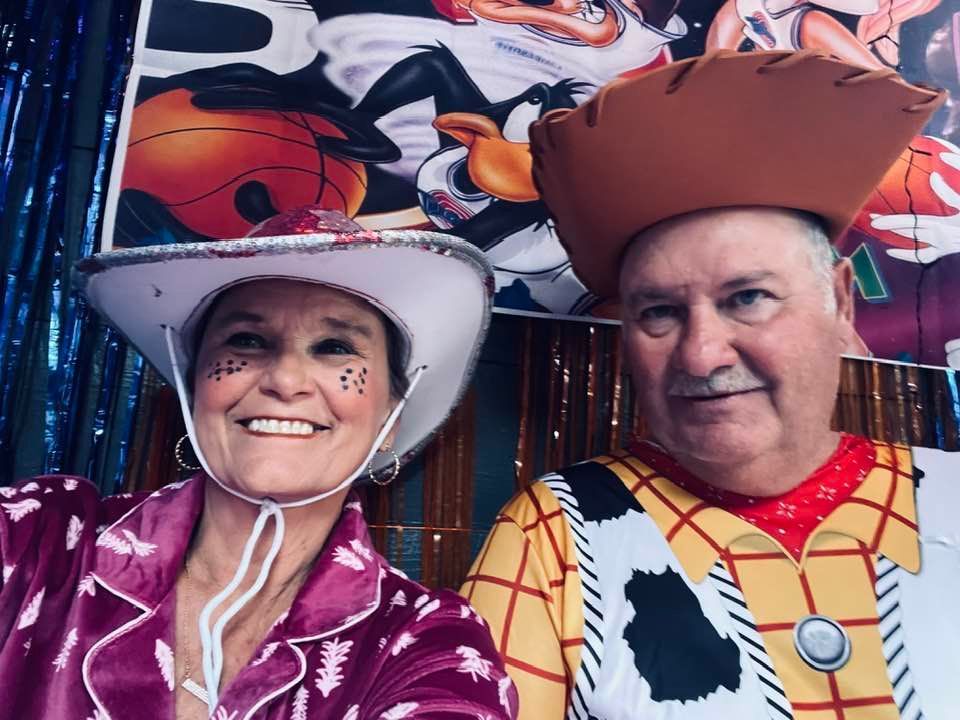 Two people in cowboy costumes smiling in front of a colorful rodeo-themed backdrop