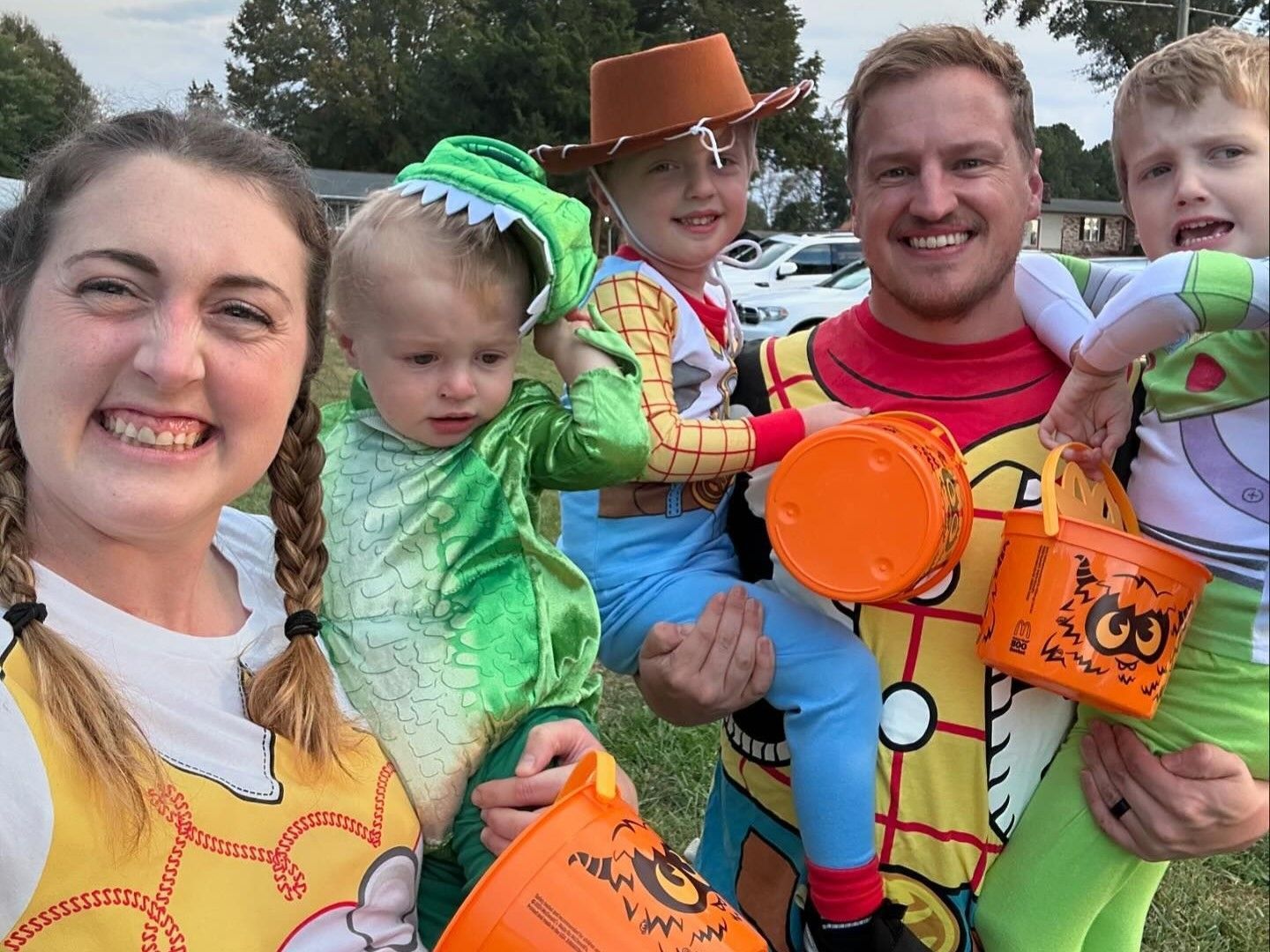 Five smiling people in colorful superhero costumes holding orange toy props outdoors