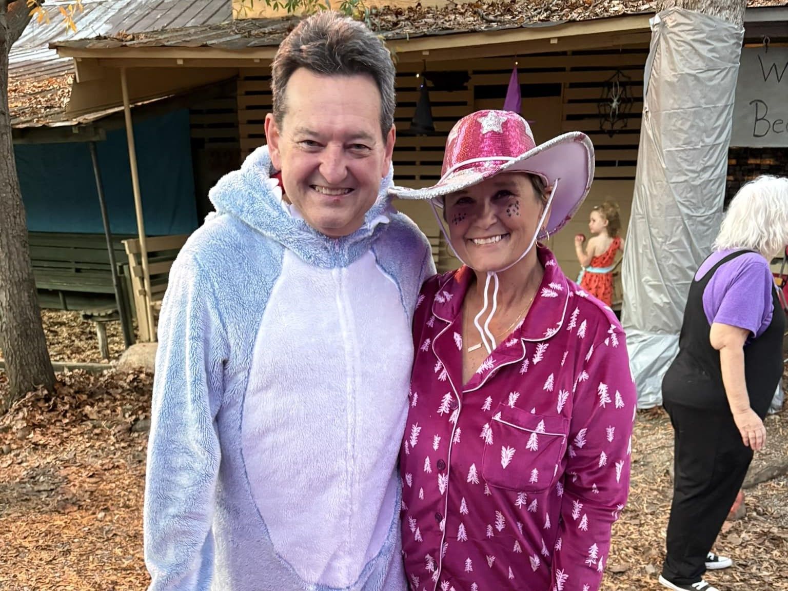 Two people smiling outdoors, one in a light purple hoodie and one in a pink cowboy hat and shirt.