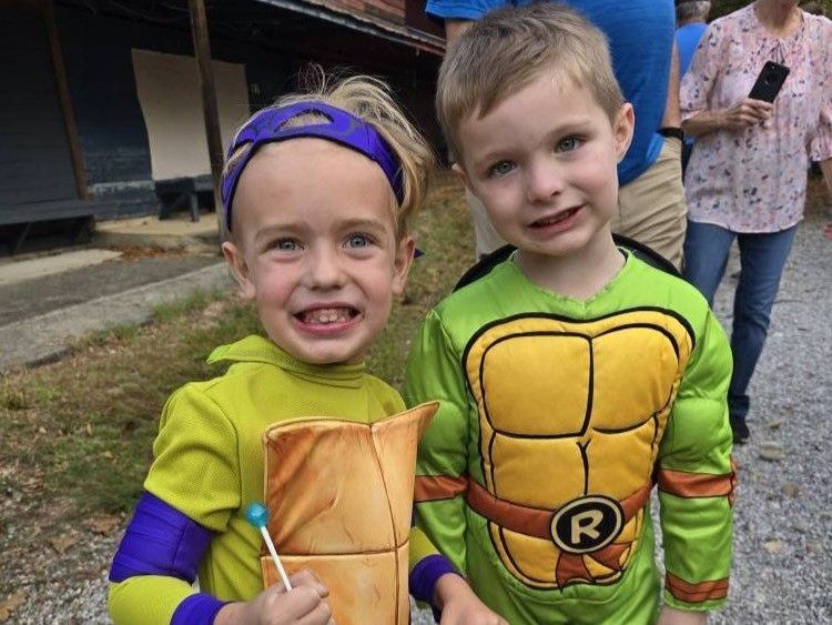Two children in turtle costumes smiling outdoors at a party