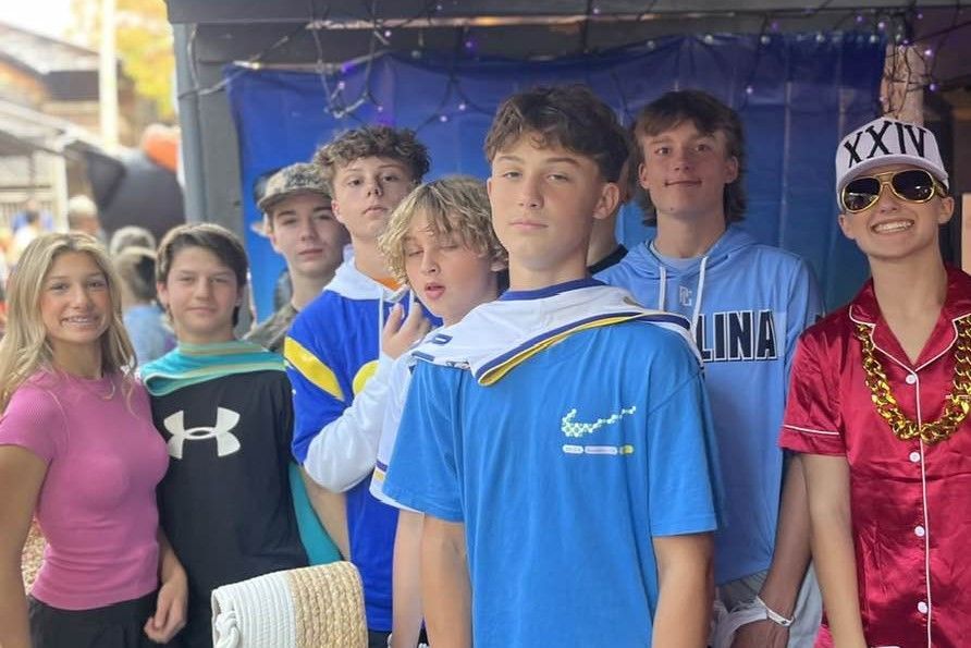 Group of people posing under a tent, wearing colorful shirts and leis, with one person in a blue cape.