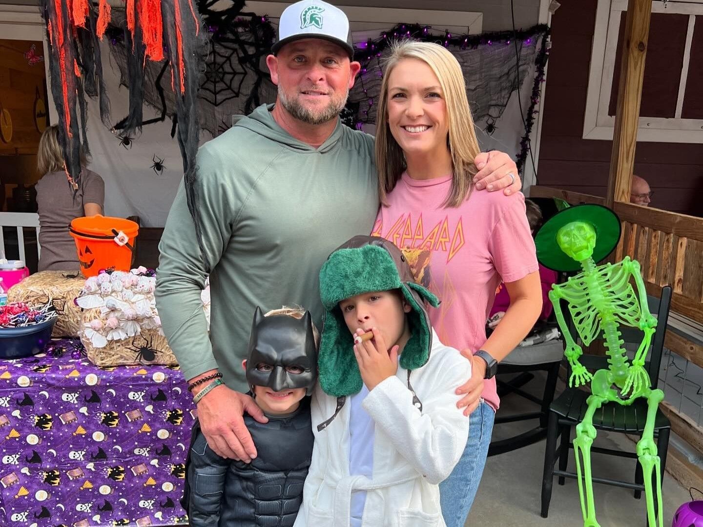 Family in Halloween costumes posing indoors with skeleton and pumpkin decorations.