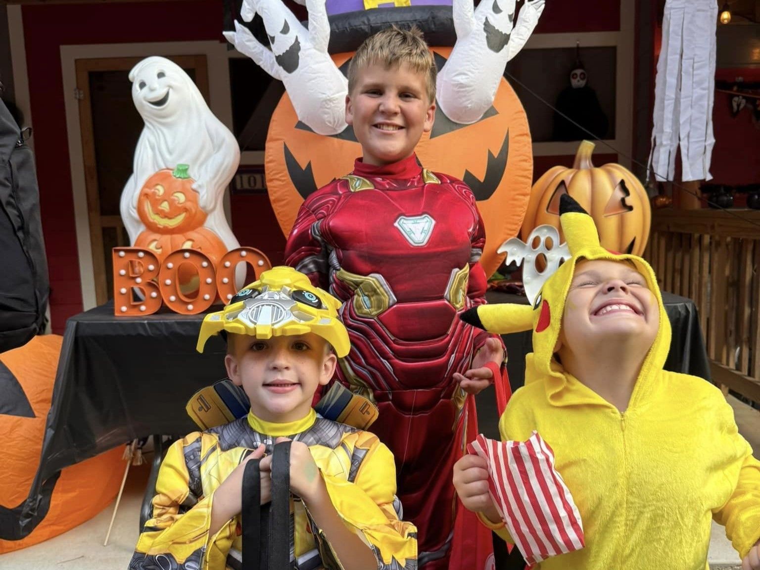 Three children in Halloween costumes posing by spooky decorations and pumpkins on a porch