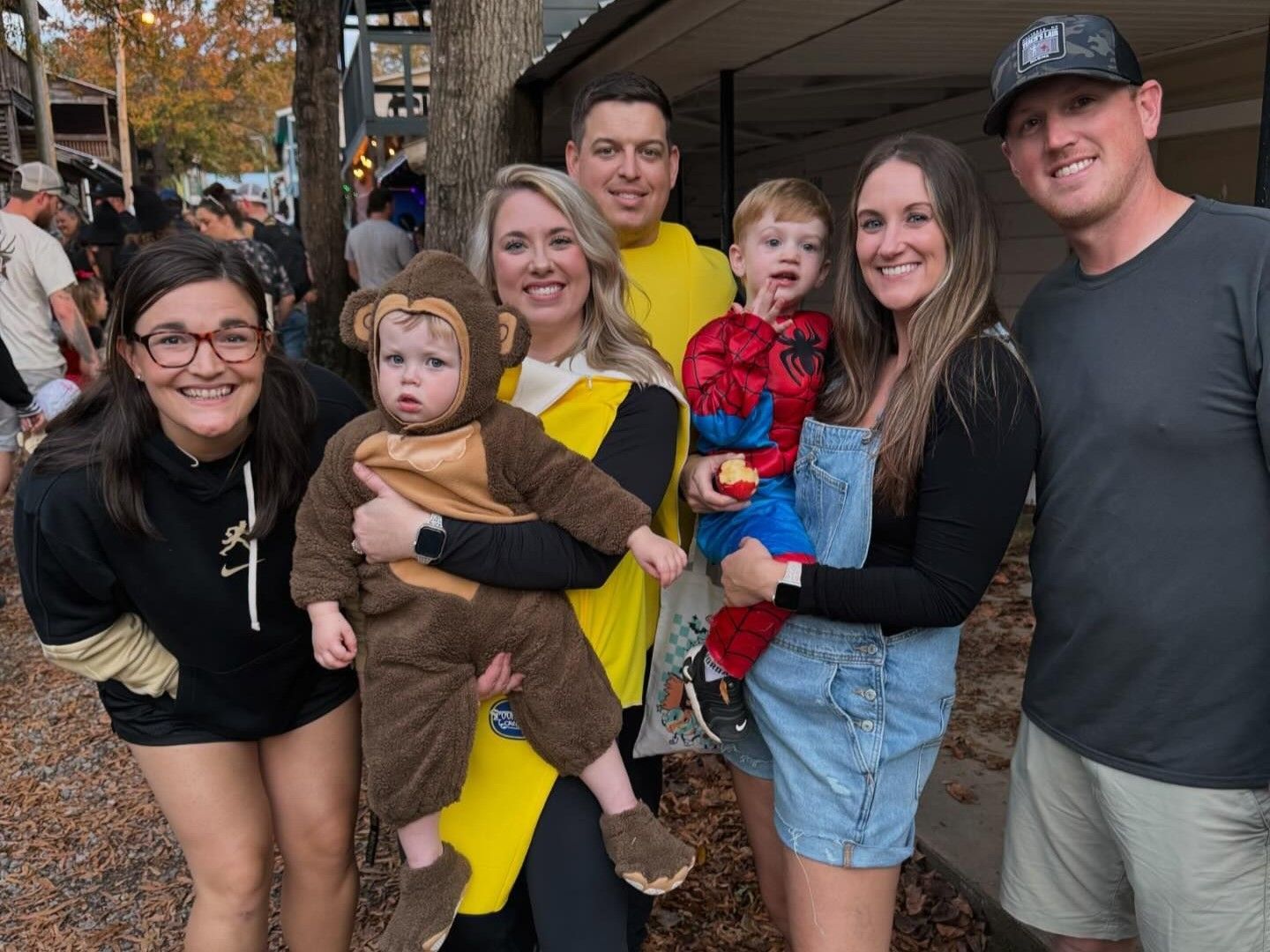 Group of six smiling people posing outdoors on a brick walkway in fall clothing.