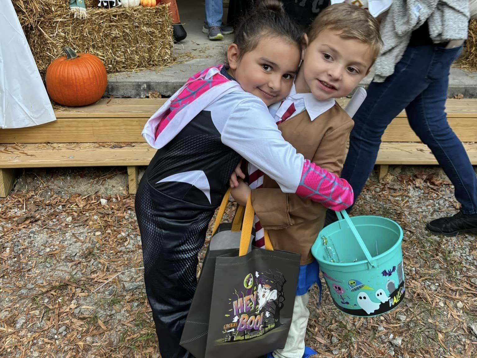 Two children hugging while holding Halloween buckets at a pumpkin display outdoors