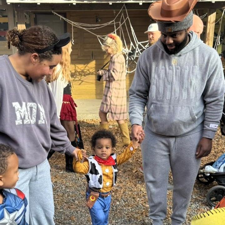 Adults and toddlers in costumes gathered outdoors at a Halloween event