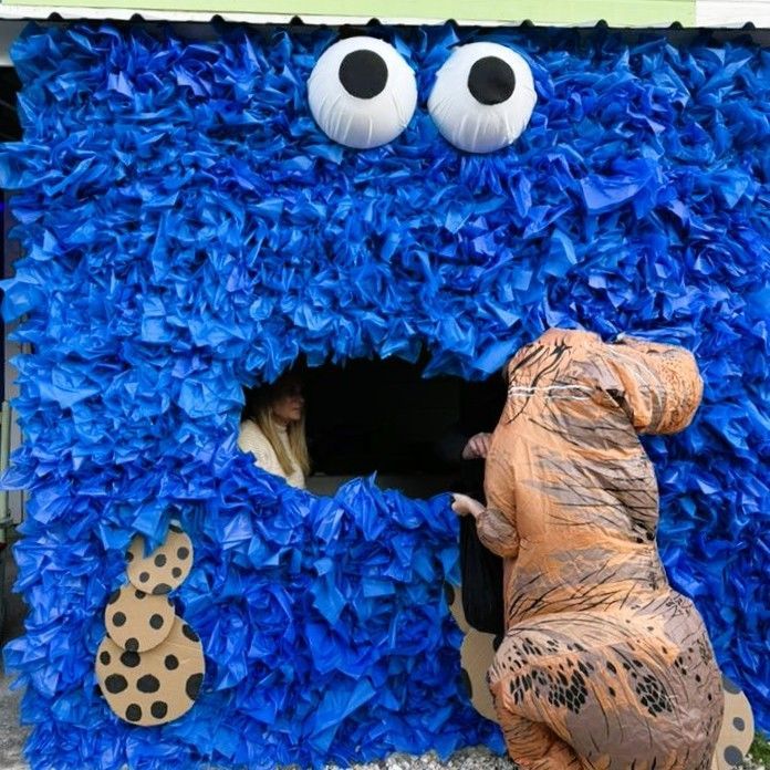 Blue fuzzy Monster Mouth booth with googly eyes; a child in a dinosaur costume reaches into the opening.