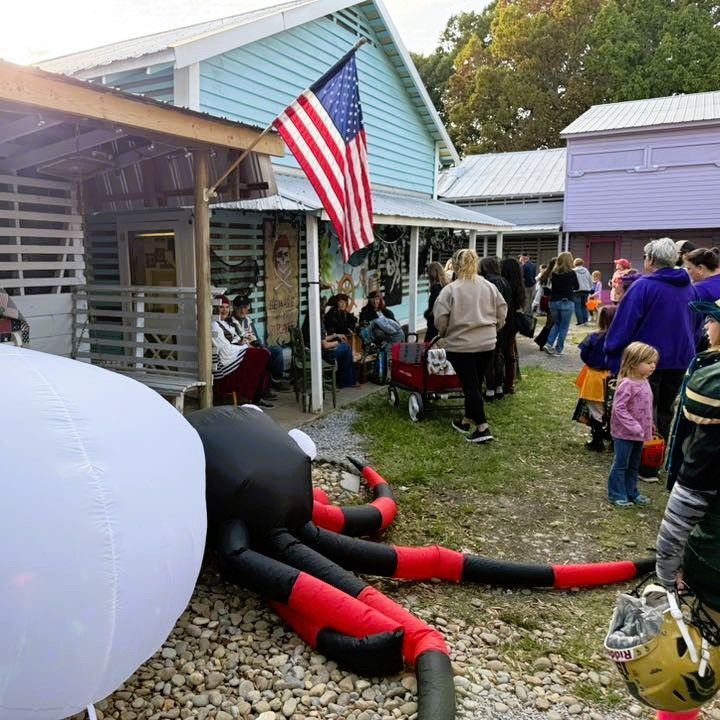 Outdoor Halloween scene with a giant inflatable spider, American flag, and people gathered by houses