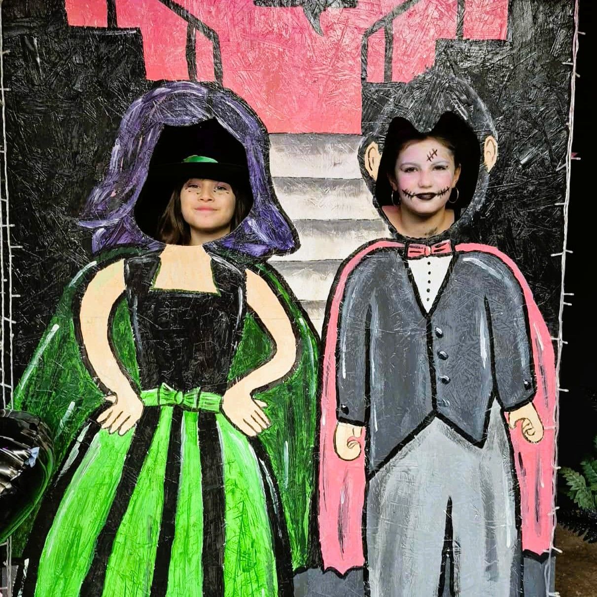 Two costumed children painted on a black background, one in a green dress and one in a gray suit with a pink cape.