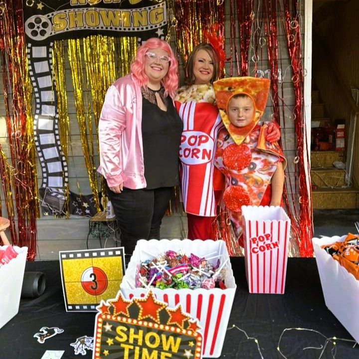 Three people posing at a popcorn stand with red-and-white striped decor and a “Show” sign