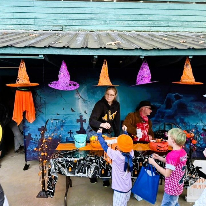 Halloween booth with hanging hats and people handing out treats to children at a decorated table
