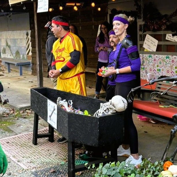 Two people in colorful outfits stand by a large outdoor grill at a festive event.