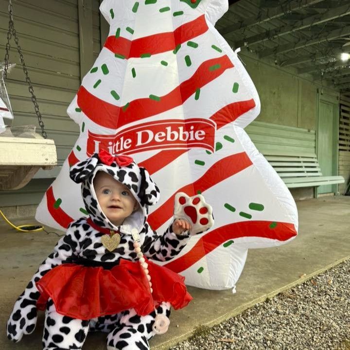 Child in black-and-white costume with red tutu posing beside a Little Debbie holiday display
