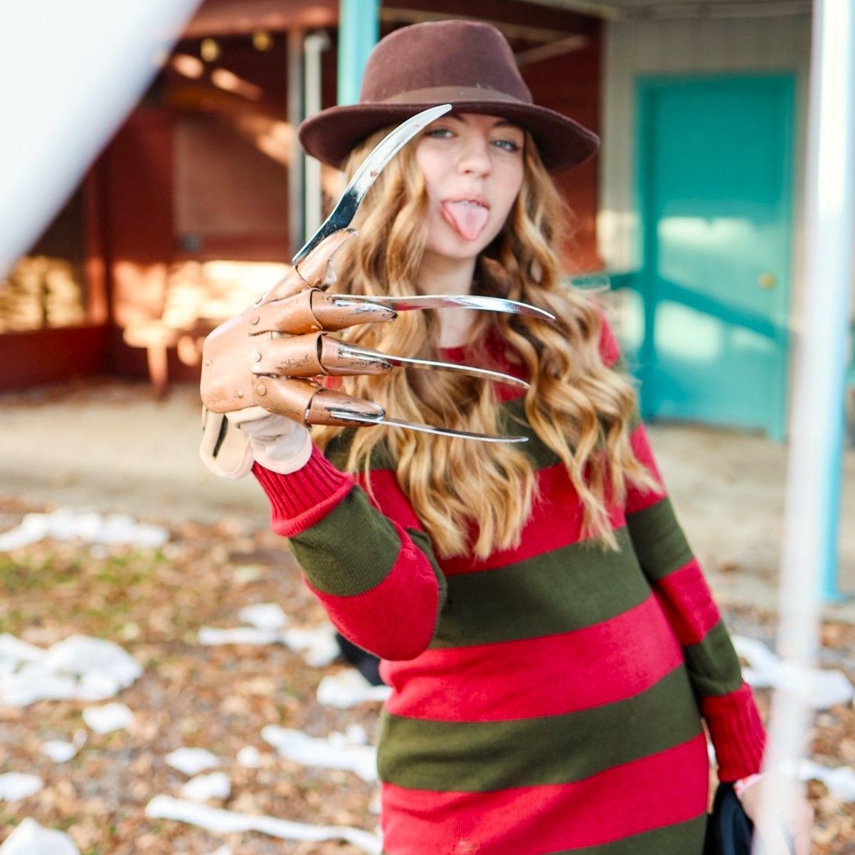Woman in a brown hat and red-green striped sweater posing outdoors with crossed fingers.