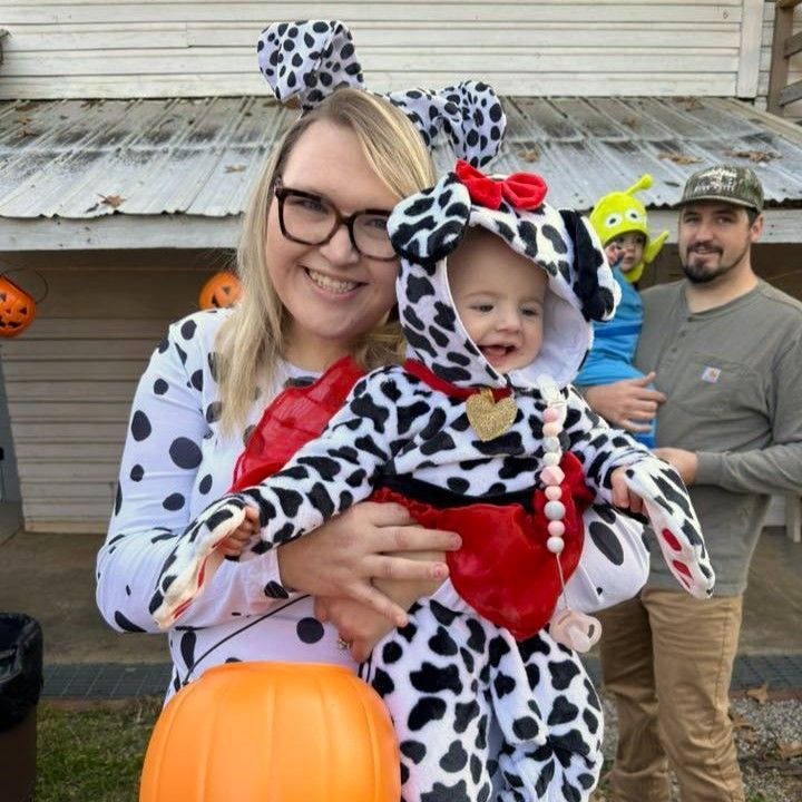 Family in spotted costumes and a pumpkin bucket posing outdoors at Halloween.