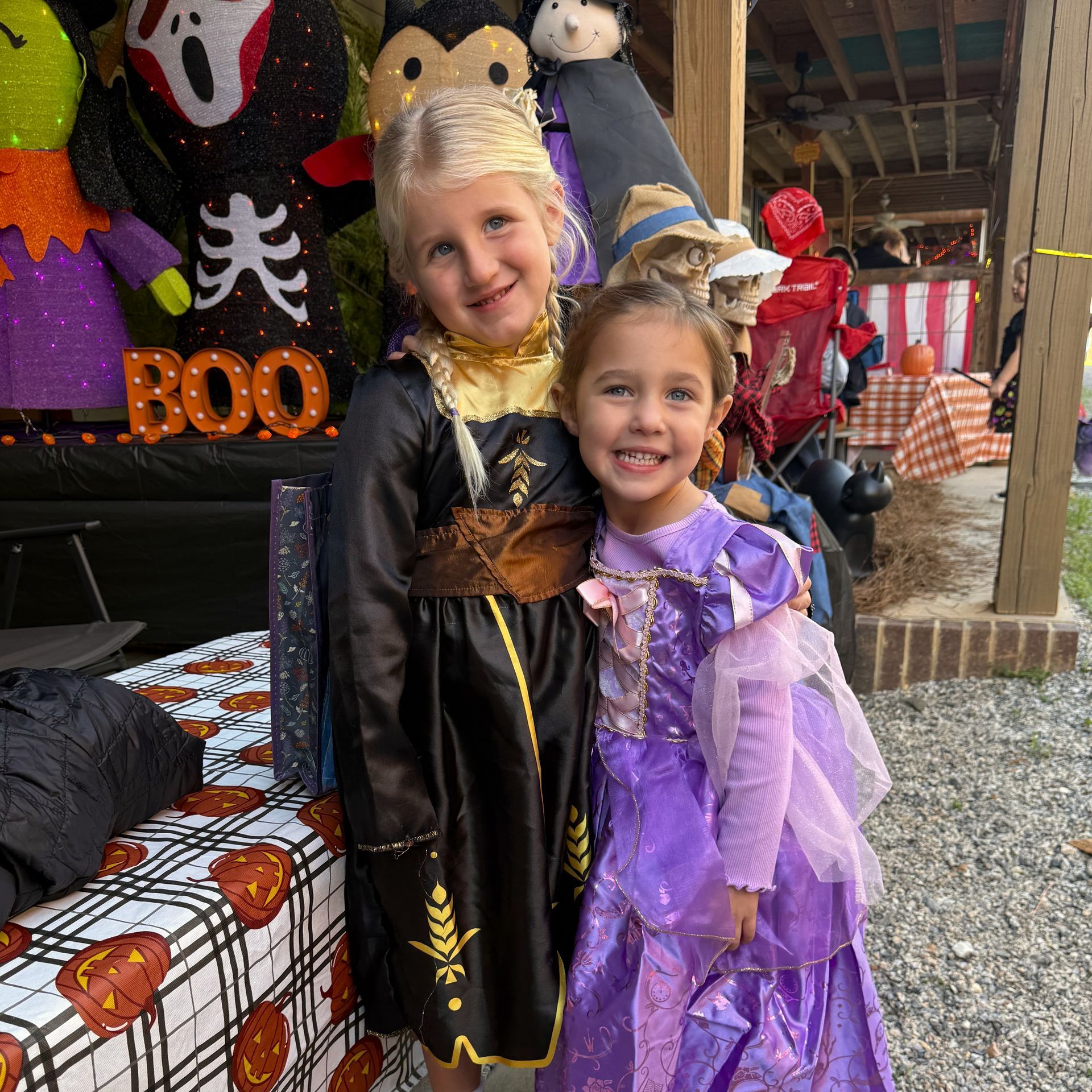 Two children in Halloween costumes smiling at a festive fall display with pumpkins and BOO decorations
