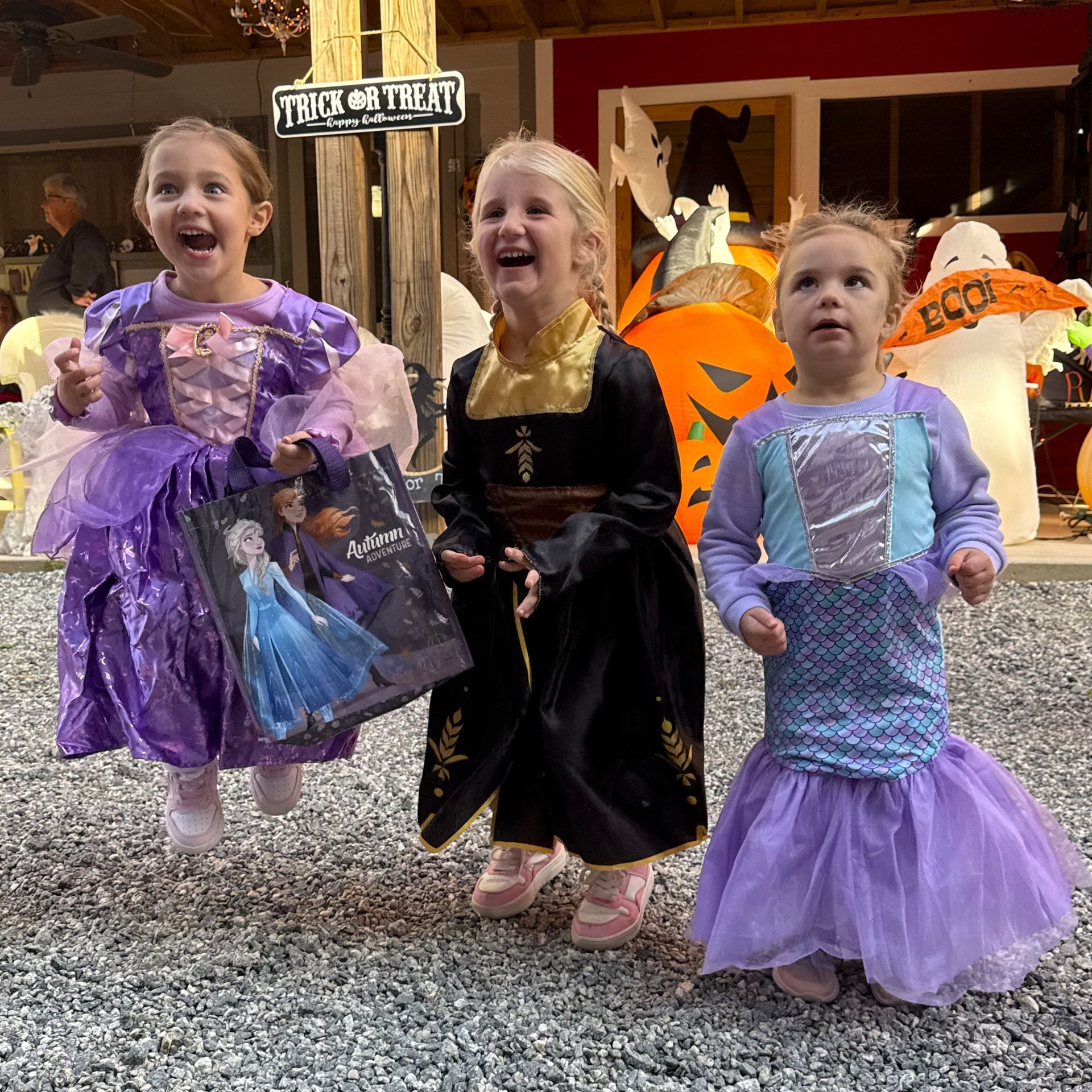 Three children in colorful princess costumes posing on a confetti-covered sidewalk outside a shop