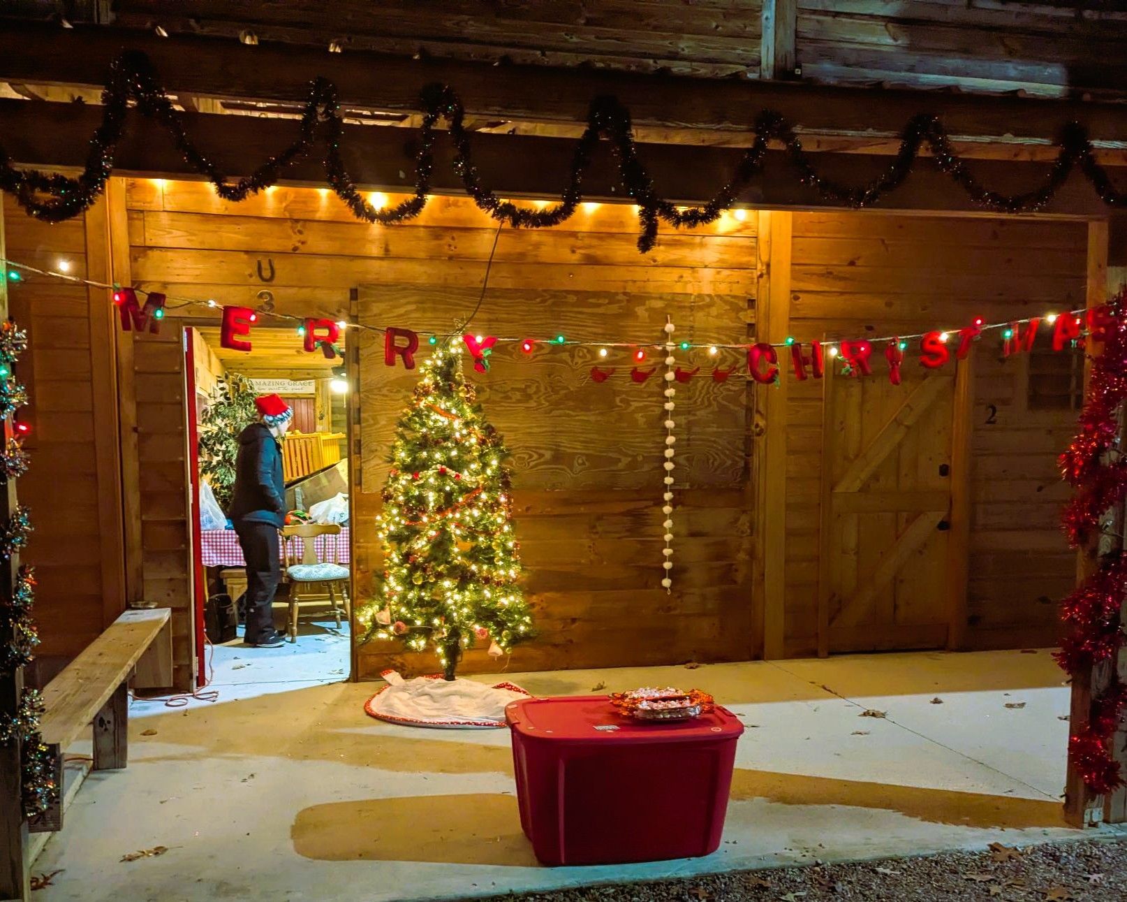 Cozy wooden cabin with a lit Christmas tree, garland lights, and a red tub in the foreground.