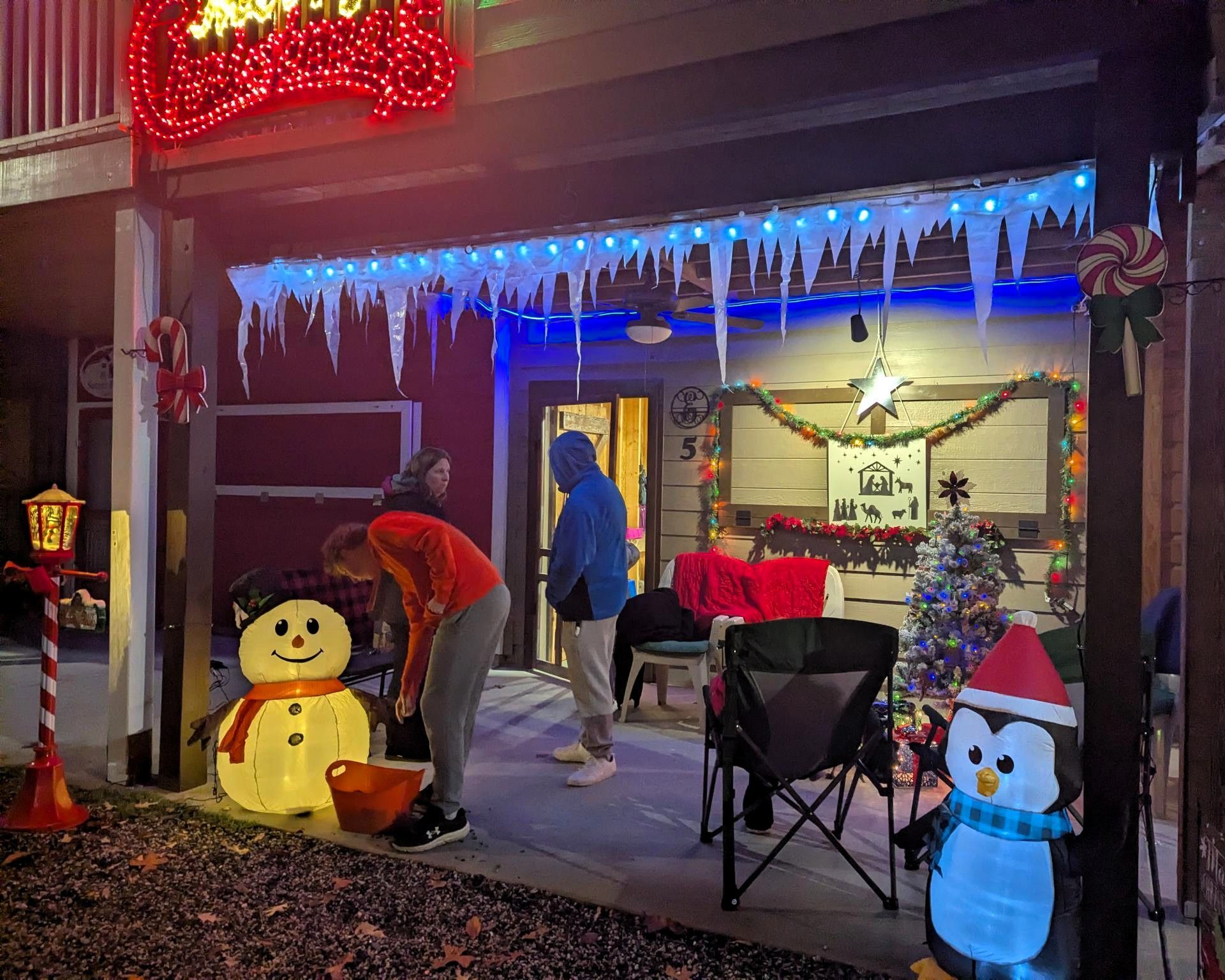 Home porch decorated for Christmas with lit inflatables, icicles, and two people arranging decorations.