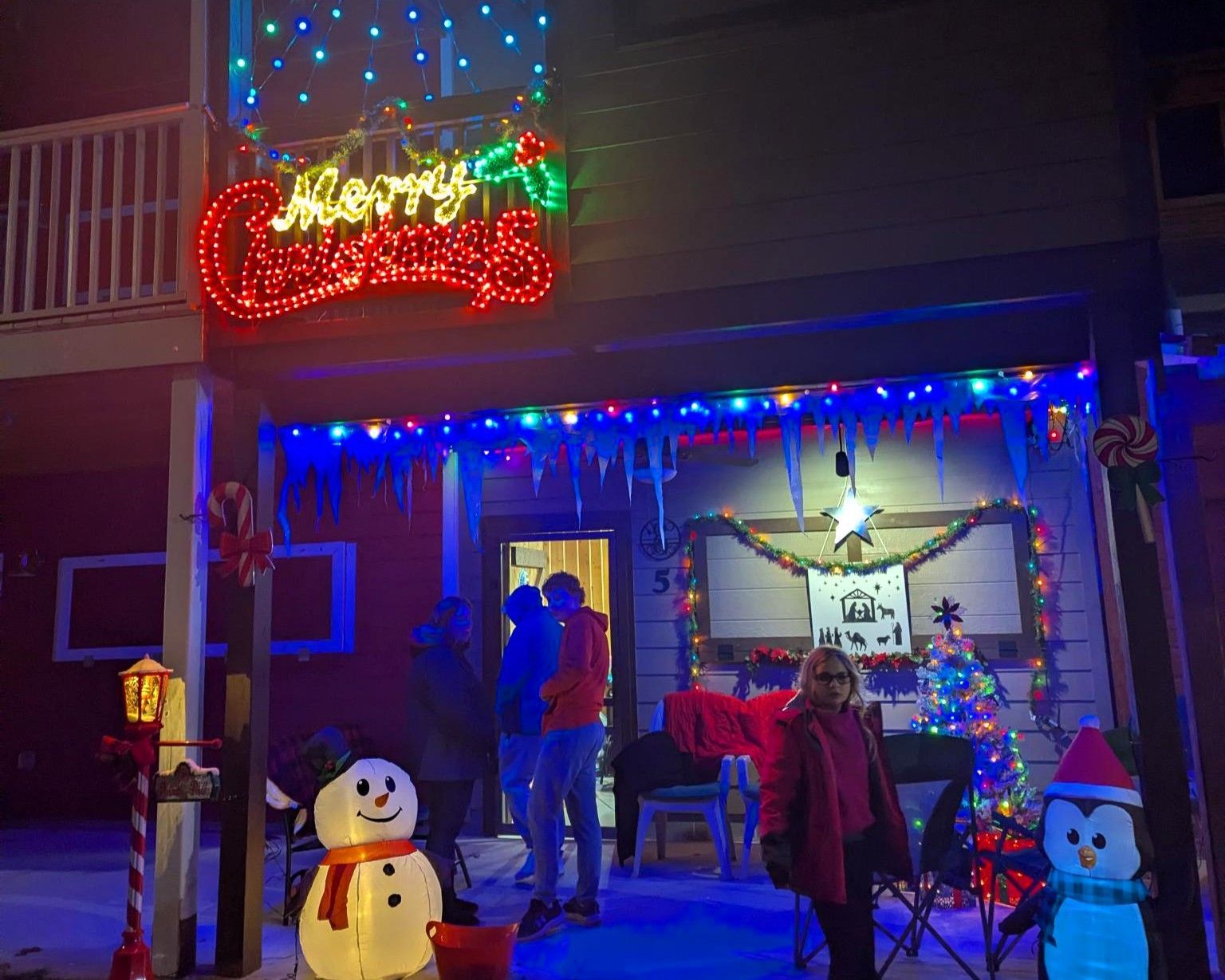 Festive house entrance with Christmas lights, snowmen, and a couple standing by the decorated doorway.