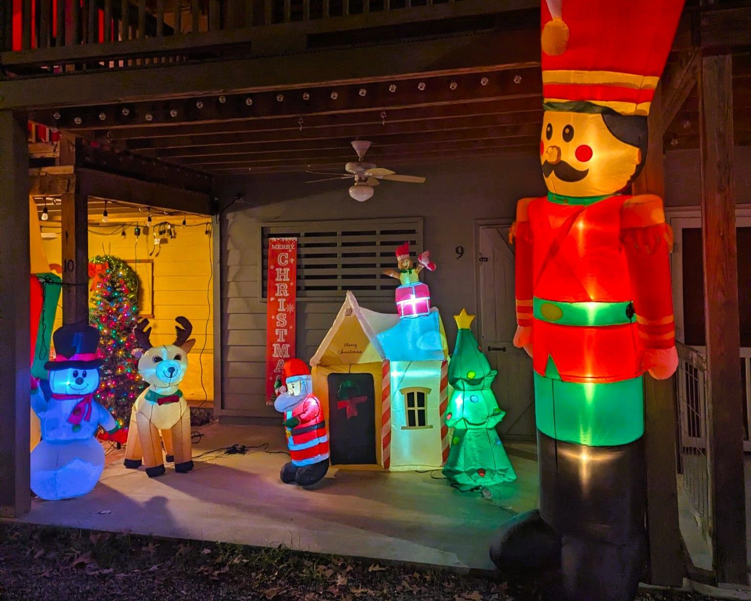 Inflatable holiday display with toy soldiers, a snowman, and a lit house on a porch at night