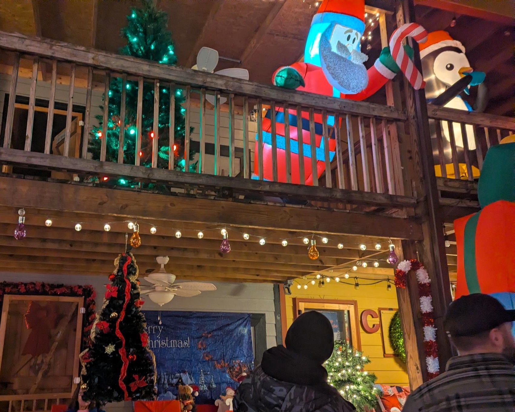 Indoor holiday display with oversized Santa and elf figures on a balcony above a decorated room