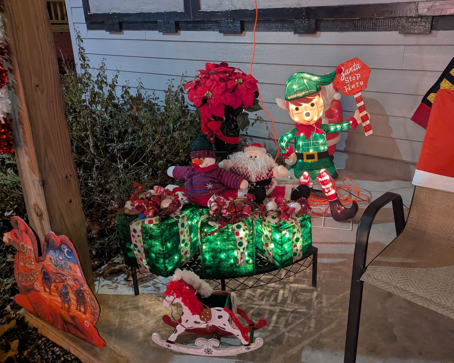 Christmas display with green gift boxes, poinsettias, and an elf figurine on a porch step