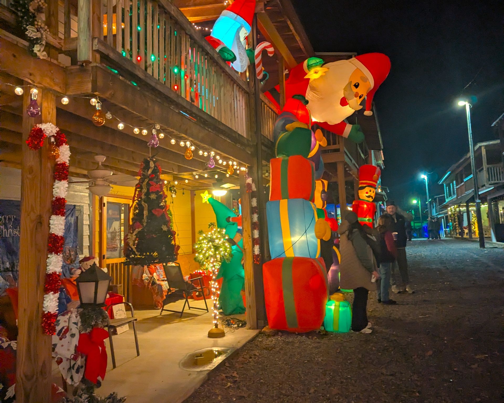 Festive street at night with lit Christmas decorations, colorful giant clown figure, and decorated storefronts